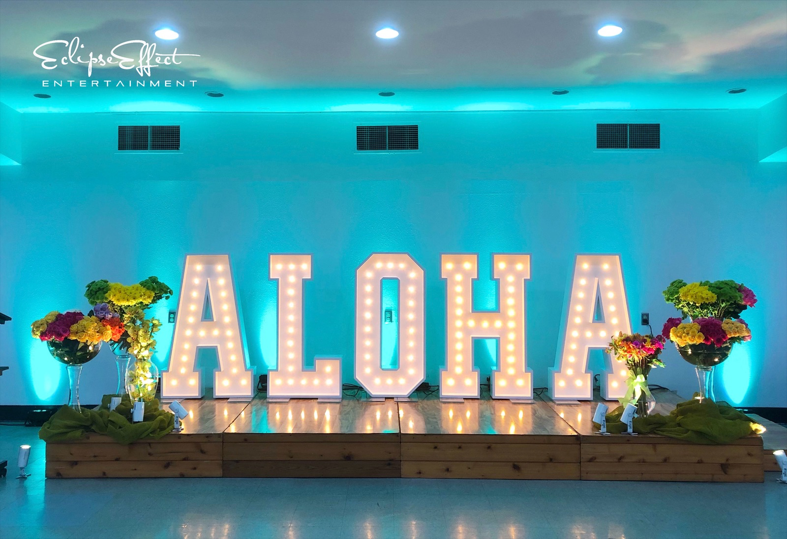 Teal uplighting behing a Aloha sign provided by Brio Photo Booth Co.